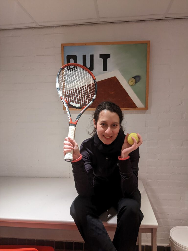 Een meisje zit onder een poster van een tennisbal die buiten de baan werpt, met een bal en haar racket vast